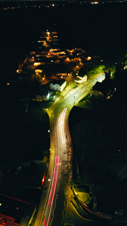Aerial night view of a curvy road with vehicle light trails connecting an illuminated town area in Knaresborough, North Yorkshire