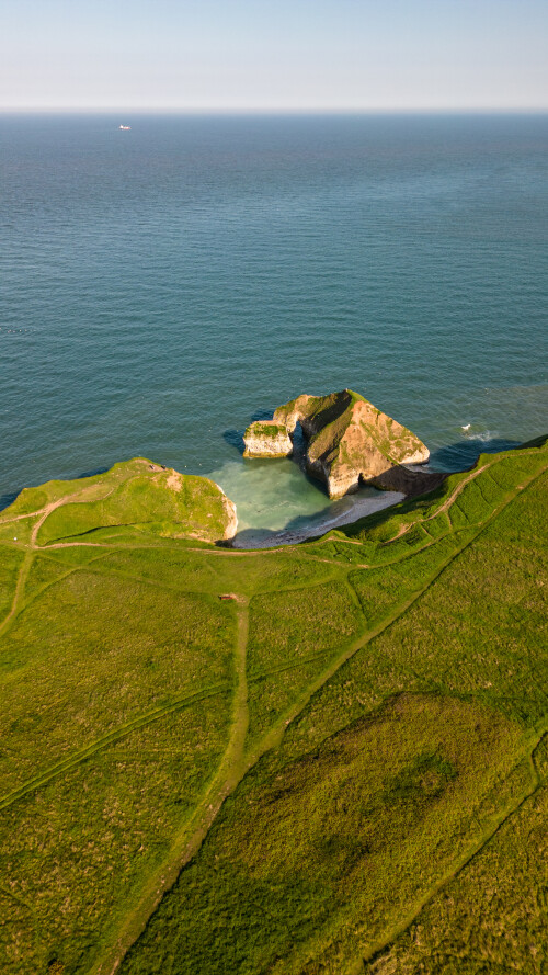 Aerial view of a lush green coastal landscape with cliffs overlooking a serene blue sea in Flamborough, England