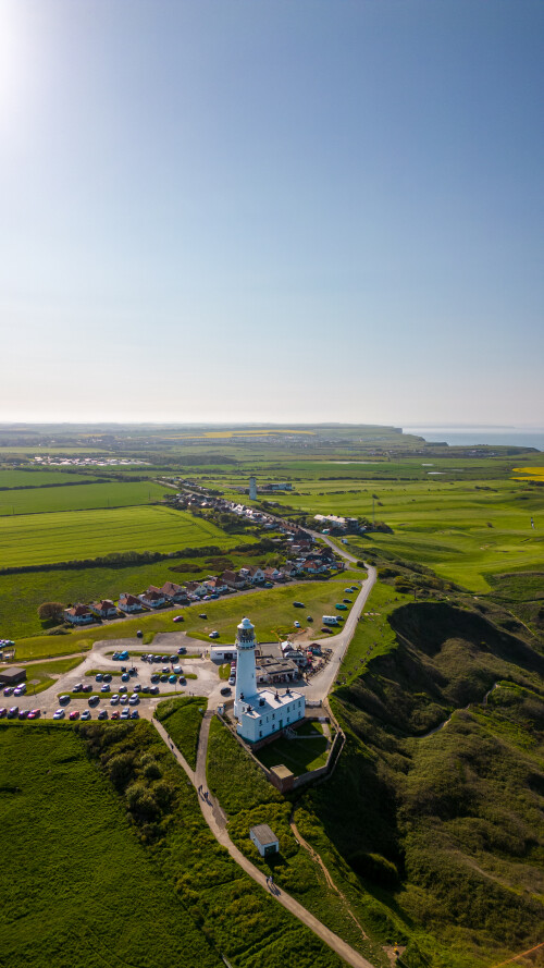 Aerial view of a coastal lighthouse with surrounding greenery and clear blue skies in Flamborough, England
