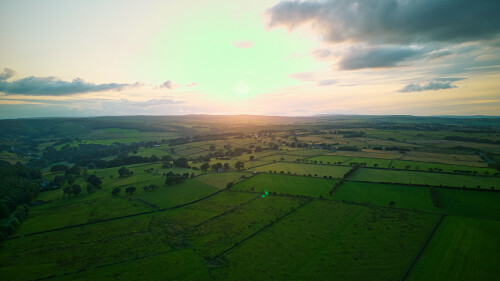 Aerial view of a lush countryside at sunset with vibrant green fields and a dramatic sky in Yorkshire.
