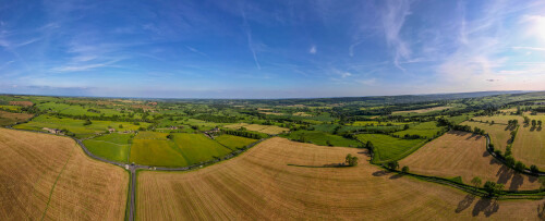 Panoramic aerial view of lush green countryside with fields and a clear blue sky.