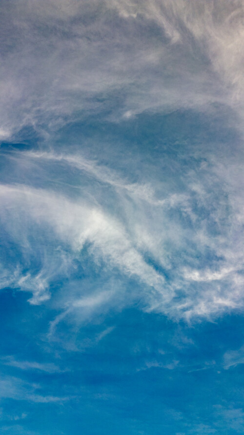 Vertical image of wispy cirrus clouds against a blue sky, depicting serene weather patterns and natural backgrounds.