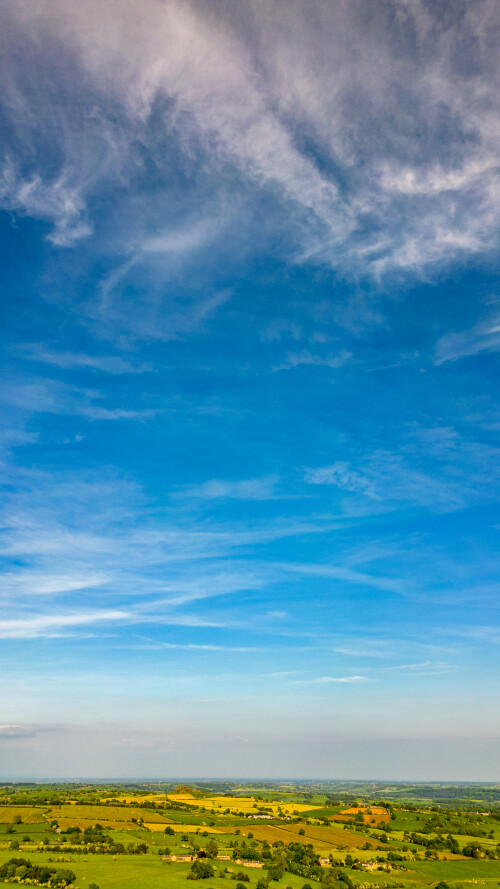 Vibrant landscape with lush green fields under a dynamic blue sky with wispy clouds.