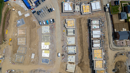 An aerial view shows a construction site with multiple foundations, scaffolding, vehicles, and building materials  at Miller Homes in Catterick, UK.