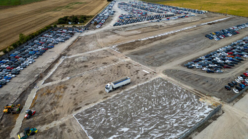 An aerial view of a large car storage lot with rows of vehicles, construction equipment, and a truck on dusty ground  at Copart yard in York, UK.