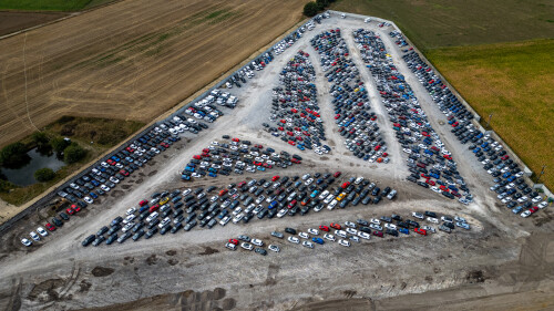 Aerial view of a vast car storage lot filled with rows of parked vehicles, bordered by agricultural fields and a small pond  at Copart yard in York, UK.