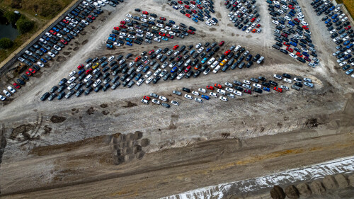 Aerial view of a vast car parking lot, filled with rows of diverse vehicles on a gravelly, dusty terrain  at Copart yard in York, UK.