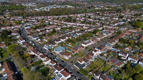 Aerial view of a densely populated suburban area with houses, roads, trees, and vehicles in Morden, London, UK.