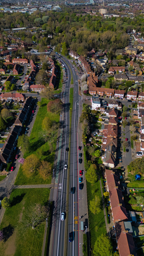 Aerial view of a road with cars passing through a suburban area with houses and trees in Morden, London, UK.