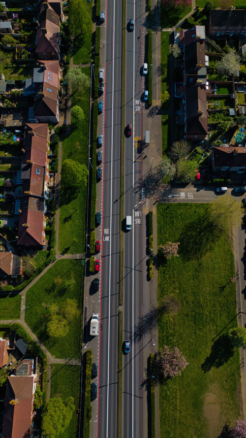 Aerial view of a multi-lane road with cars, bordered by houses and green spaces in Morden, London, UK.