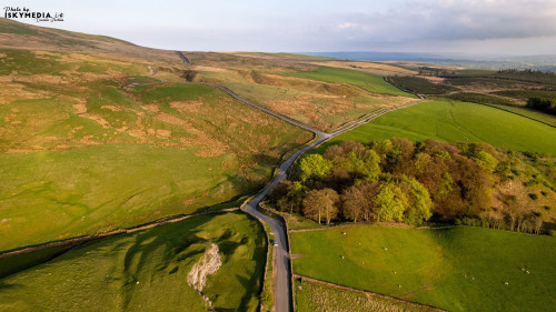 Aerial view of a winding road through lush green countryside with rolling hills under a soft evening sky.
