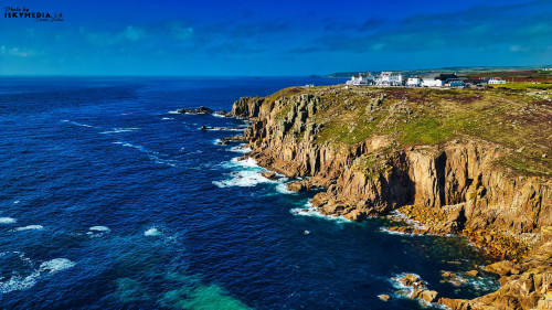 A stunning coastal view featuring rugged cliffs and a vibrant blue ocean. The scene captures the natural beauty of the shoreline with waves crashing against the rocks, under a clear sky.
