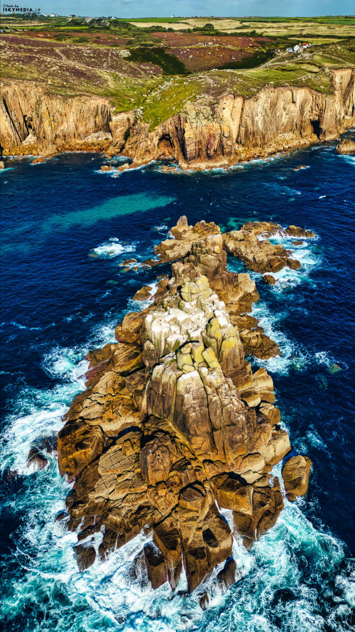 Aerial view of a rocky coastline with waves crashing against the rocks. The landscape features rugged cliffs and vibrant blue ocean water, showcasing the natural beauty of the coastal environment.