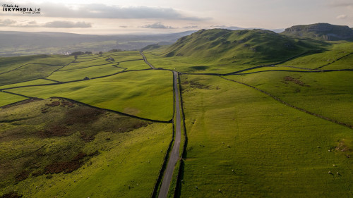 Aerial view of a winding road through lush green rolling hills under a soft light at dawn or dusk.