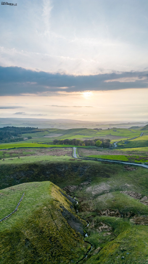 Scenic vertical landscape with rolling hills and a sunset over a tranquil countryside.