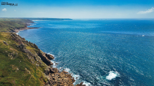 A stunning coastal view showcasing rugged cliffs and a vast blue ocean under a clear sky. The shoreline features rocky formations and lush greenery, with gentle waves lapping against the rocks. The horizon is dotted with distant ships, creating a serene and picturesque landscape.