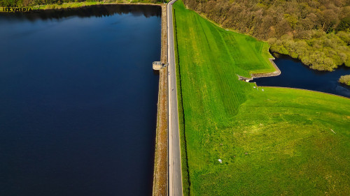 Aerial view of a dam separating a river and a lush green field, showcasing the contrast between water and land.