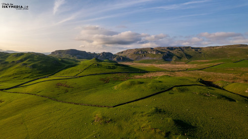 Aerial view of a lush green valley with winding paths and rolling hills under a clear sky.