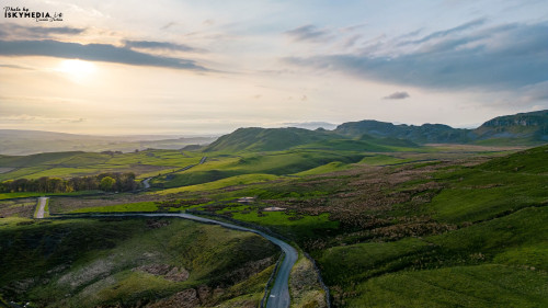 Scenic view of a winding road through lush green hills with a sunset backdrop.