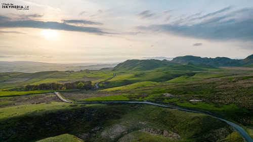 Scenic view of a winding road through lush green hills with a dramatic sky at sunset.
