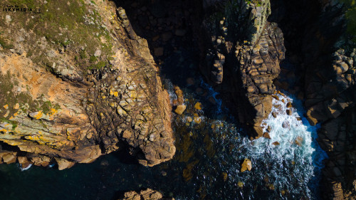 Aerial view of rocky coastline with waves crashing against the rocks. The image captures the contrast between the rugged terrain and the deep blue sea, showcasing the natural beauty of the shoreline.