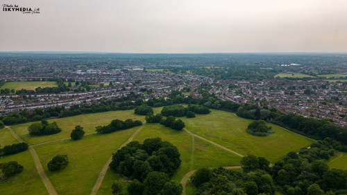 Aerial view of a green urban park surrounded by a dense residential area under a hazy sky in London.