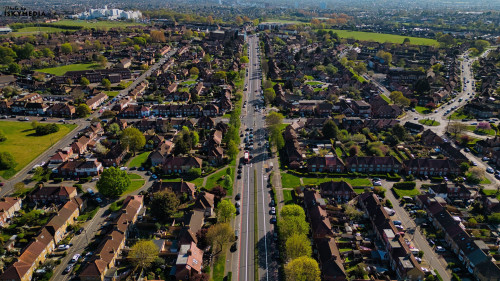 Aerial view of a suburban area featuring rows of houses bisected by a main road with traffic in Morden, London, UK.