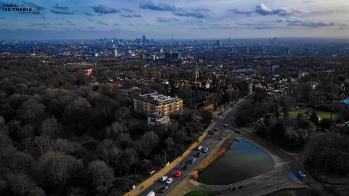 Aerial view of a city skyline at dusk with urban park, water bodies, and scattered clouds.