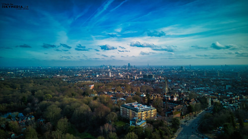 Aerial view of a city skyline with lush greenery under a vibrant blue sky with wispy clouds.