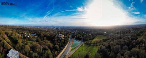 Panoramic aerial view of a lush green landscape with a road under a bright blue sky with wispy clouds.