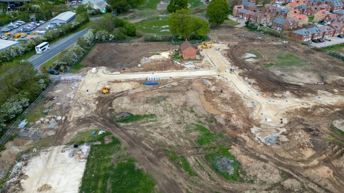 Aerial view of a construction site with earth mounds, fencing, and surrounding urban environment at Bellway Homes in Boroughbridge, UK.