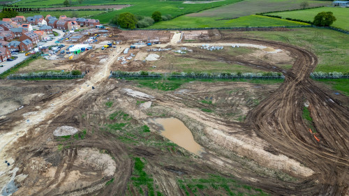 Aerial view of a construction site with dirt, machinery, and surrounding residential area at Bellway Homes in Boroughbridge, UK.
