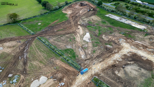 Aerial view of a construction site with dirt mounds, machinery, and surrounding greenery at Bellway Homes in Boroughbridge, UK.