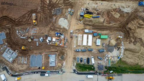 An aerial view of a construction site with various vehicles, materials, and partially built structures at Bellway Homes in Boroughbridge, UK.