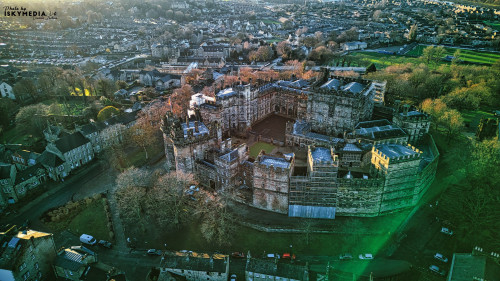 Aerial view of a historic Lancaster castle at sunset with surrounding greenery and urban backdrop.