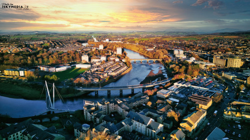 Aerial view of a city Lancaster at sunset with a river, bridges, and warm lighting.