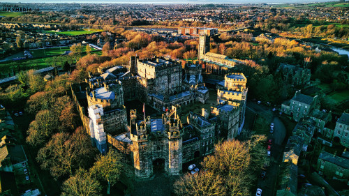 Aerial view of the Lancaster Castle amidst lush trees during sunset, with a panoramic backdrop of a quaint town.