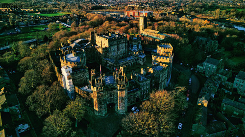 Aerial view of the Lancaster castle surrounded by greenery at sunset, showcasing the architecture and landscape.