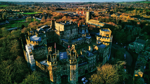 Aerial view of the Lancaster castle surrounded by lush greenery in a quaint town during sunset.