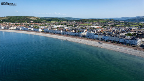 Aerial view of a picturesque coastal town with a long sandy beach and row of buildings along the shore in Llandudno, North Wales.