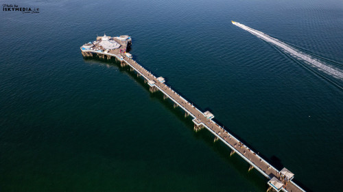 Aerial view of a pier extending into the ocean with a speedboat leaving a trail behind in Llandudno, North Wales.